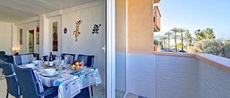 A dining area with a table set for four, a balcony with a view of palm trees and buildings, and decorative wall art.