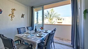 Ein Essbereich mit Tisch für vier Personen, Stühlen, einer Wanddekoration und Blick auf Palmen und Gebäude durch das Fenster.