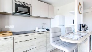 Une cuisine moderne avec des meubles blancs, un four à micro-ondes encastré, une machine à café et un petit coin repas comprenant deux chaises et une table.