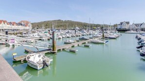Un port de plaisance où sont amarrés de nombreux bateaux, avec des passerelles en bois et, au fond, des bâtiments aux toits rouges.