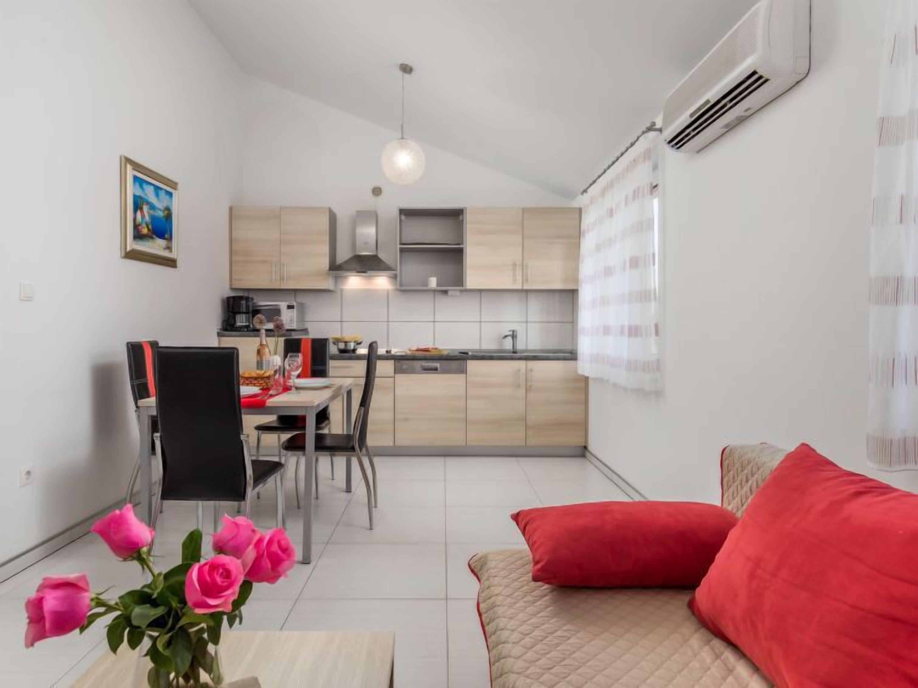 A compact living space with a kitchenette, dining area, and a sofa with red cushions.