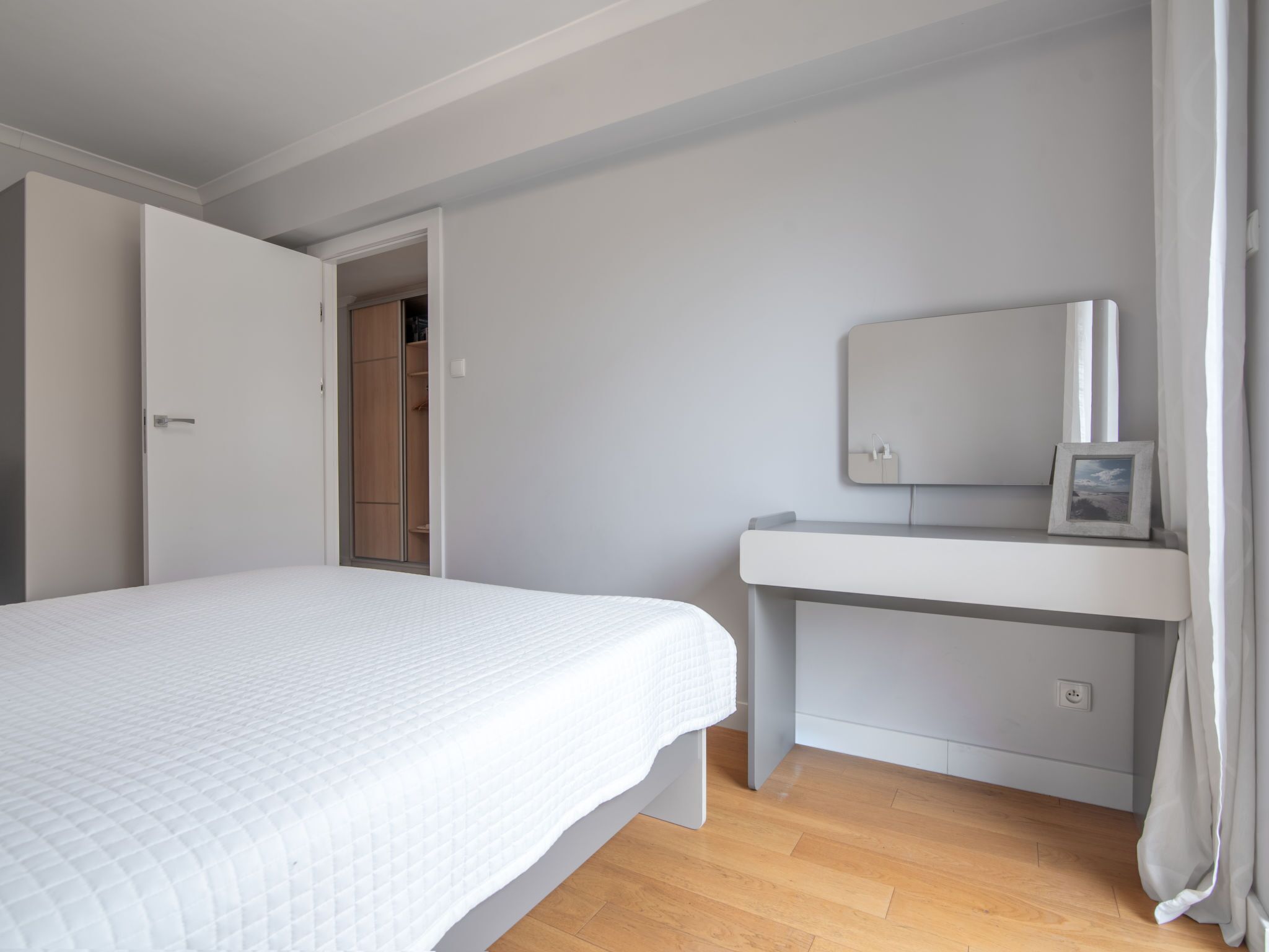 Een slaapkamer met een bed, nachtkastje, spiegel en kledingkast.