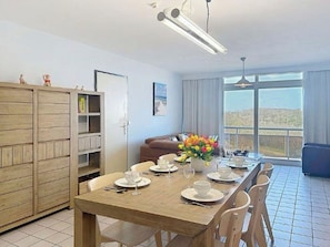 A dining area with a wooden table set for four, a vase of flowers, and a view through large windows.