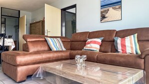 Un canapé en cuir marron agrémenté de coussins à rayures, une table basse en bois et un tableau sur le thème de la plage accroché au mur.