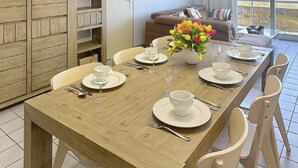 Un coin repas avec une table en bois dressée pour quatre personnes, des chaises, un buffet et un canapé en arrière-plan.