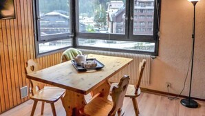 Habitación de esquina con una mesa de madera, sillas, un radiador y vistas a edificios a través de amplios ventanales.