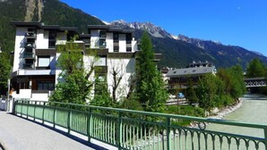 Un hotel moderno con varios pisos, un río al frente y montañas al fondo.