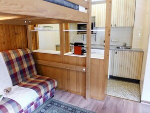 Une pièce compacte comprenant un lit superposé, un coin cuisine et un petit espace salon.