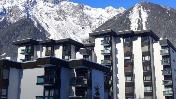 Un hotel moderno con varios pisos y balcones, frente a imponentes montañas nevadas.