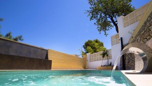 Une piscine à l’eau claire, un mur de pierre et un arbre.