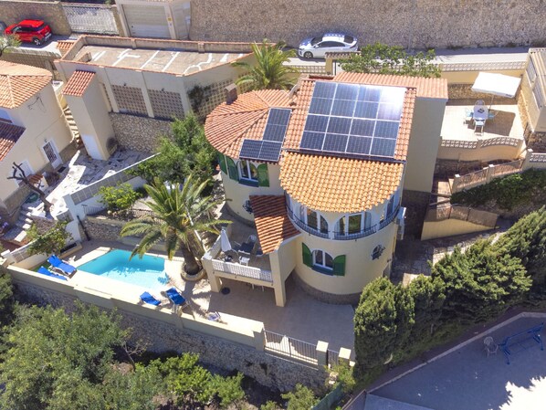 A multi-story building with a swimming pool, solar panels, and a patio area.