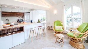 Une cuisine moderne avec des armoires blanches, un comptoir en bois et un ventilateur de plafond. On y trouve deux chaises vertes et un petit tabouret dans l’espace repas.