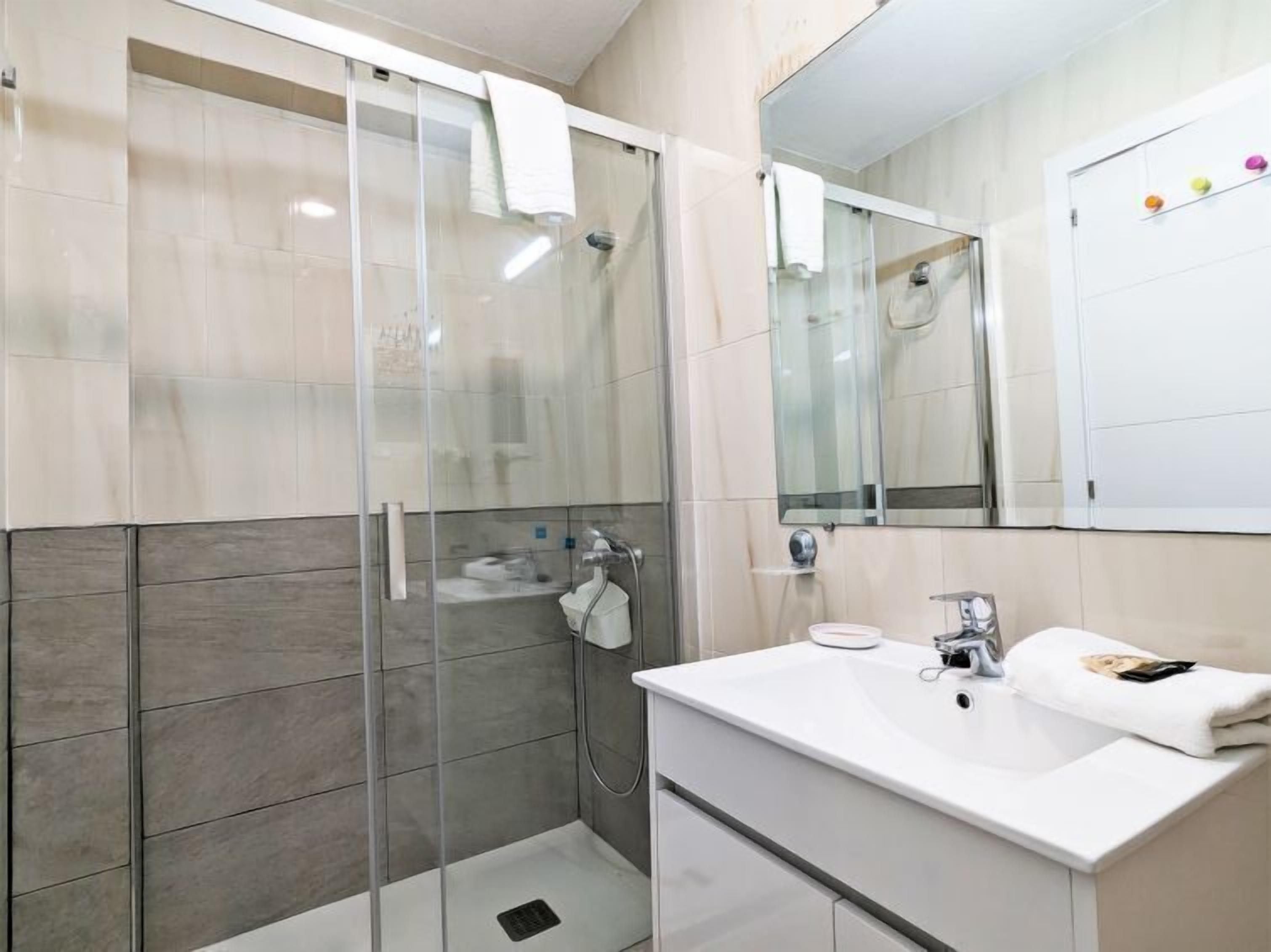 A modern bathroom with a glass-enclosed shower, a white sink, and a large mirror.