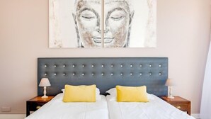 Una cama doble con cabecera capitonada, dos mesitas de noche con lámparas, y un cuadro abstracto de gran tamaño sobre la cama.