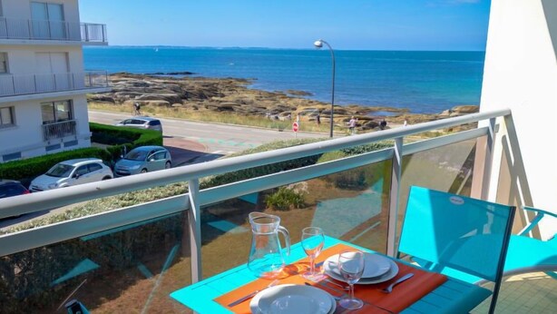 Un balcón con una mesa lista para dos personas, con vistas a un litoral rocoso y al mar.