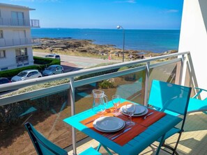 En balkon med et bord dækket til to, med udsigt over en klippefyldt kystlinje og havet.