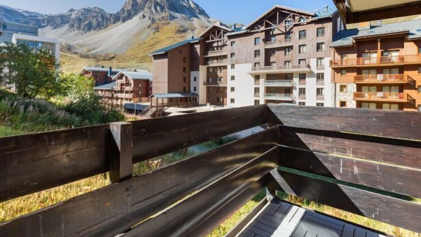 A wooden deck overlooking a mountainous area with modern buildings in the background. - Le Pramecou (Val Claret) by Interhome (Tignes)