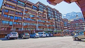 Un hotel de varios pisos con balcones, estacionamiento y montañas al fondo.