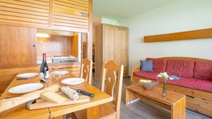 Una mesa de comedor de madera con platos, una botella y un rodillo. Un sofá rojo y un armario de madera se ven al fondo.
