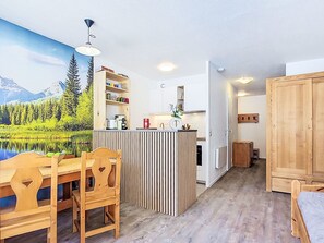 Une pièce chaleureuse avec une table à manger en bois, des chaises, un coin cuisine équipé d’un évier et de placards, et une grande fenêtre offrant une vue panoramique.