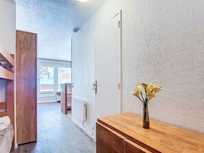 A hallway with a wooden cabinet, a vase with flowers, and a door leading to another room. - Névés 150 by Interhome (Val Thorens)