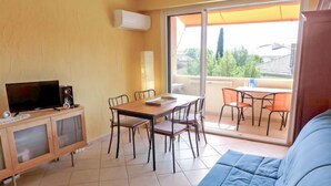 A living area with a sofa, a TV, and a dining table with chairs. - Les Vignes by Interhome (Saint Cyr sur mer Les Lecques)