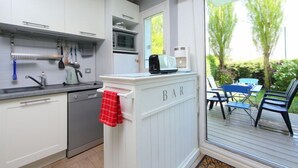 A modern kitchen with white cabinets, a built-in microwave, and a bar area with a red towel. - Le Garden by Interhome (Cabourg)