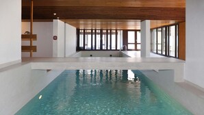Ein großes Hallenbad mit klarem Wasser, Holzbalkendecke und großen Fenstern, die für natürliches Licht sorgen.