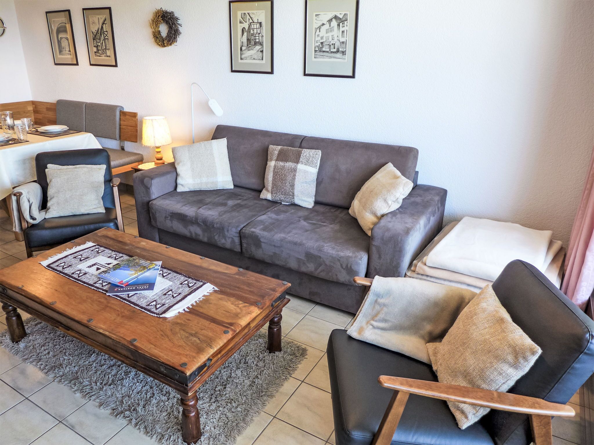 Un salon avec un canapé gris, deux fauteuils, une table basse en bois et une table à manger avec des chaises.