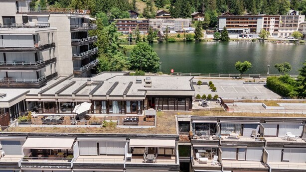 Ein modernes Hotel mit mehreren Etagen, Außenbereichen zum Sitzen und Blick auf einen See.