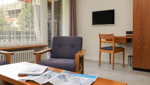 A room with a wooden desk, a chair, a television on the wall, and a window with a view of buildings and trees. - Matten (Utoring) by Interhome (Zermatt)
