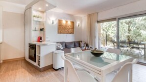 A modern living room with a glass dining table, white chairs, a sofa, and a kitchen area with a coffee machine. - Cala Sultana by Interhome (Porto Vecchio)