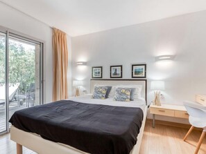 Una camera da letto moderna con un letto grande, una scrivania e una sedia. Sono presenti due comodini con lampade, una porta scorrevole in vetro verso l'esterno e tre quadri appesi al muro.