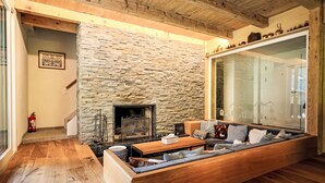 A cozy living room with a stone fireplace, wooden flooring, and a built-in sofa. - Chalet Butz by Interhome (Grindelwald)