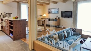 A cozy living room with a wooden ceiling, a dining area with a table and chairs, a kitchen with modern appliances, and a large window providing natural light. - Chalet Butz by Interhome (Grindelwald)