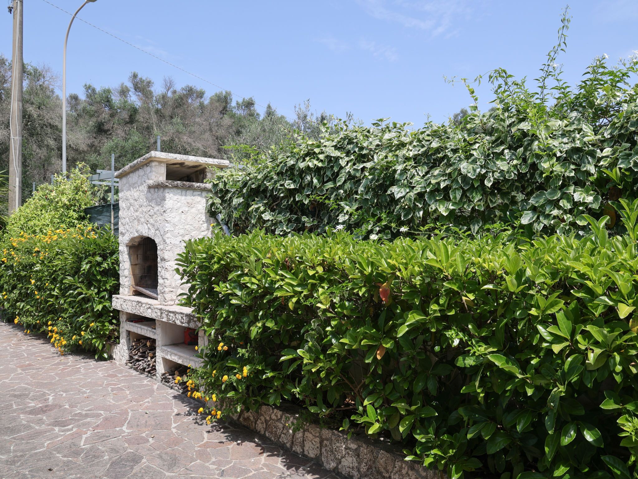 A stone pathway leading to a stone structure with an arched entrance, surrounded by lush green hedges and flowering plants.