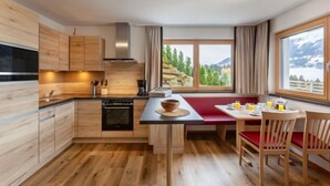 Cozinha moderna com armários de madeira, forno embutido e área de refeições com um banco vermelho e cadeiras de madeira.