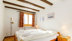A bedroom with a wooden bed, a nightstand, a red rug, and a window with curtains. - Apartment Apt.17 by Interhome (Silvaplana-Surlej)