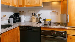A kitchen with wooden cabinets, a dishwasher, a coffee maker, a kettle, and a stove. - Apartment Apt.17 by Interhome (Silvaplana-Surlej)
