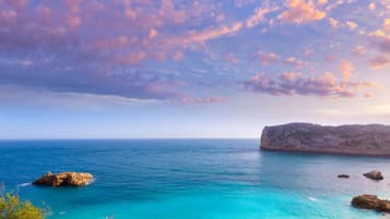 Un paisaje costero con cielo despejado, una gran formación rocosa y mar tranquilo.