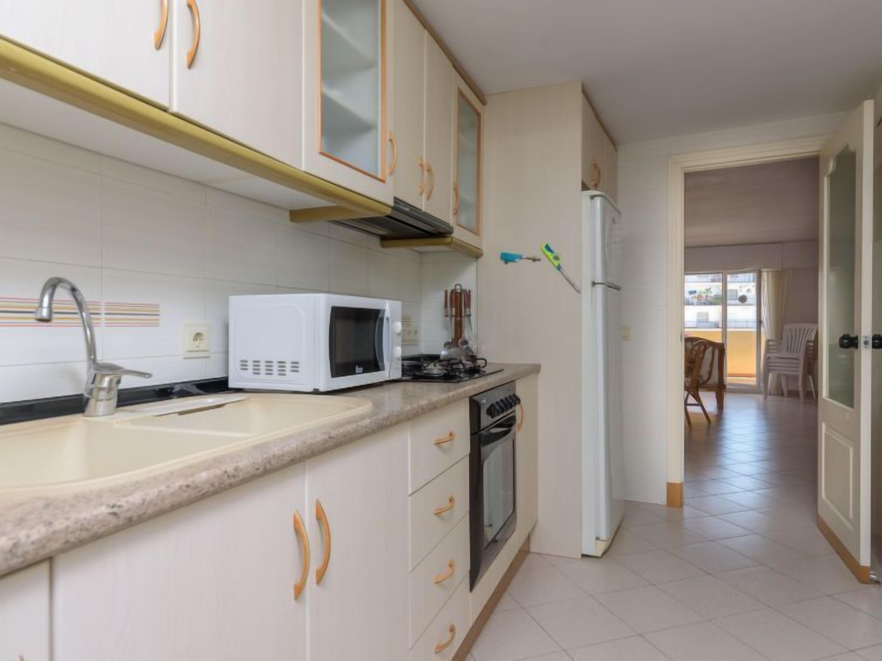 A kitchen with white cabinets, a microwave, a sink, and a refrigerator.