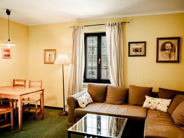 A living room with a wooden table, two chairs, a sofa with cushions, a floor lamp, and a window with curtains. - Apartment Chopin by Interhome (Marianske Lazne)