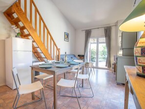 A modern kitchen with a wooden staircase, a dining area with a table set for four, and a view of the outdoors through a sliding glass door.
