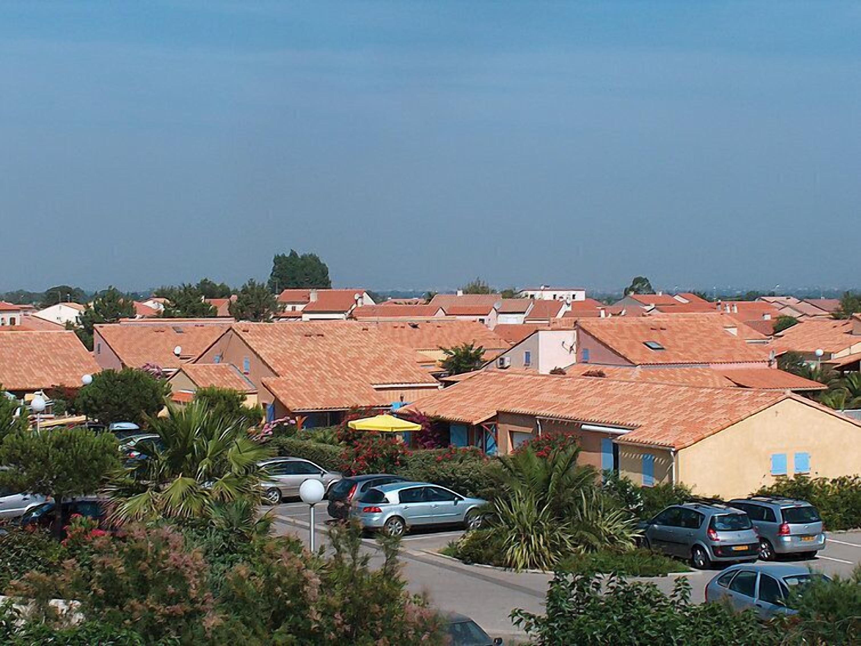 A residential area with terracotta-roofed houses, parked cars, and lush greenery.