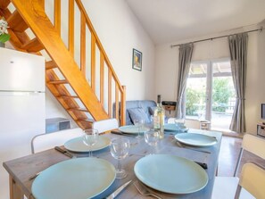 A dining area with a wooden staircase, a table set for four with blue plates and wine glasses, and a bottle of wine on the table.