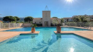 Piscina azul cristalina com dois grandes vasos, rodeada por um deck ladrilhado e um cercado branco.