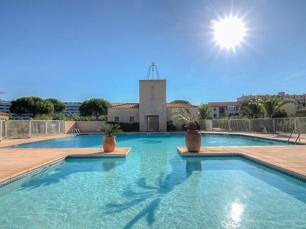 A clear blue swimming pool with two large planters, surrounded by a tiled deck and a white fence.
