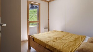 Ein Schlafzimmer mit einem hölzernen Bett, Blick ins Grüne durch eine Glastür und einer Deckenleuchte.