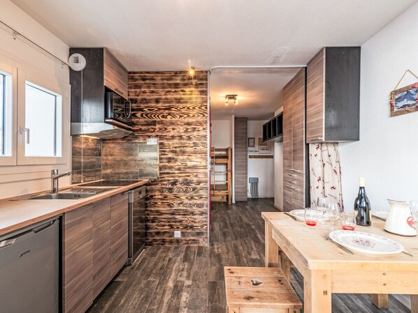 A modern kitchen with wooden cabinetry, a built-in stove, and a dining area with a wooden table set for two. - Plein Soleil (Val Claret) by Interhome (Tignes)