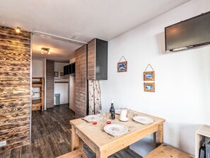 A modern kitchen with wooden cabinets, a dining table set for two, and a flat-screen TV mounted on the wall. - Plein Soleil (Val Claret) by Interhome (Tignes)